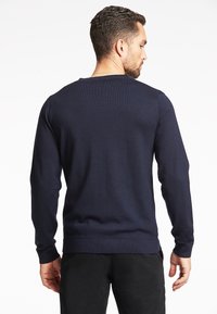 Maglione a coste blu navy con maniche lunghe, scollo a giro e vita aderente. Texture liscia senza motivi o loghi visibili.
