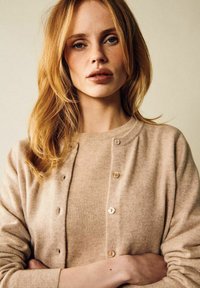Beige cardigan i mjukt tyg, med knäppning fram, rund halsringning och långa ärmar. Slät textur med subtila detaljer.