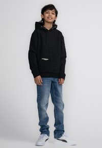 Felpa nera con cappuccio e motivo testuale in rilievo, tasca frontale, abbinata a jeans azzurri chiari e sneakers bianche. Design semplice e casual.