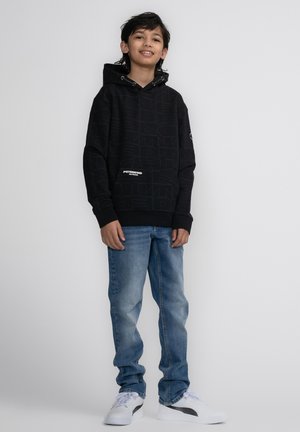 Zwarte hoodie met reliëftextuur, voorzak, gecombineerd met lichtblauwe spijkerbroek en witte sneakers. Eenvoudig, casual ontwerp.