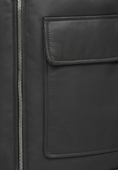 Čierna kožená bunda s strieborným zipsom, hladkou textúrou a náprsníkou so šitými okrajmi, ktorá zdôrazňuje minimalistické dizajnové detaily.