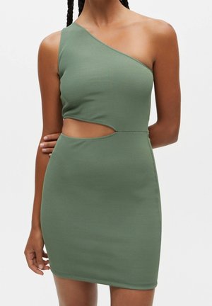 Femme portant une robe moulante en côte olive verte à une épaule, avec une découpe au niveau de la taille et un ourlet court, sur un fond uni.