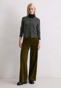 Cardigan en tricot gris avec un col rond et des boutons sur le devant, associé à un pantalon en velours côtelé olive à jambes larges et des bottes à plateforme noires.