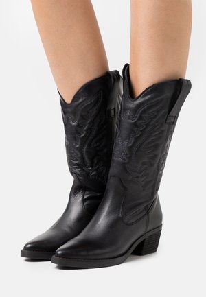 Stivali da cowboy in pelle nera con punte appuntite, dettagli di cuciture intricate, tacco quadrato di altezza media e bordi smerlati.