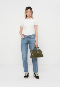 Λευκή μπλούζα κοντό μανίκι, ανοιχτό μπλε τζιν ψηλής μέσης και πράσινη τσάντα χειρός με λεπτομέρεια αστέρι. Το μοντέλο φοράει μαύρα παπούτσια sneakers με λευκά κορδόνια.