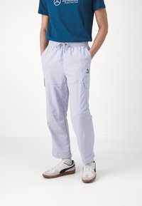Lichtpaarse cargo-broeken met een elastische taille, zijzakken en het Puma-logo. Gecombineerd met witte sneakers met grijze en blauwe accenten.