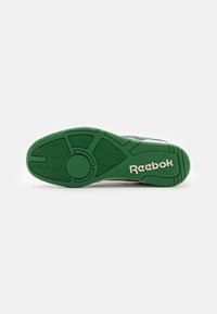 Grön gummisula med en strukturerad mönster, med en cirkulär accent och "Reebok"-logotyp i vitt. Designad för grepp och hållbarhet.