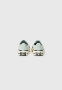 Light blue canvas slip-on shoes featuring a rubber sole, white midsole, and black branding on the heel. Back view showcases minimal design.
