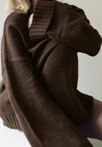 Rjav pleten oversized pulover z rebrastim ovratnikom in manšetami, ki ima teksturirano površino in sproščen kroj.