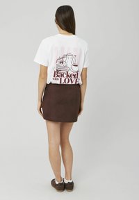 T-shirt blanc avec un motif graphique représentant des aliments et le texte "Cuit avec AMOUR." Jupe marron en suédine synthétique, chaussures marron décontractées.