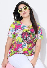 T-shirt coloré à manches courtes ornée de motifs abstraits de graffiti rose, jaune et vert, avec un cœur en imprimé léopard et un design de visage souriant.