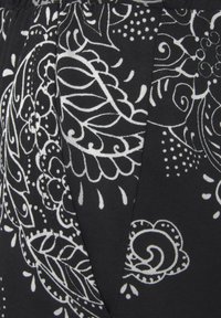 Zwarte stof met ingewikkelde witte bloemen- en paisleypatronen, gedetailleerd lijnwerk en stipaccenten, zachte textuur met een lichte glans.