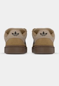 Μπεζ πάνινα παπούτσια από σουέτ με καφέ λάστιχο σόλας, που διαθέτουν μαύρο λογότυπο στο πίσω μέρος, στρογγυλεμένο σχήμα και υφασμένη λεπτομέρεια στη φτέρνα.