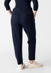 Navy jogger-housut, joissa on joustovyötärö, kaksi takataskua ja kapeat lahkeet. Yhdistetty valkoisiin ja beigeihin lenkkareihin.