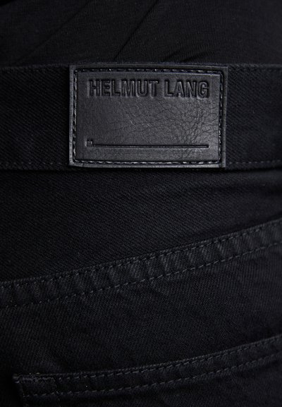 Tissu en denim noir avec une étiquette en cuir embossée "HELMUT LANG". La couture est noire et la texture est lisse.