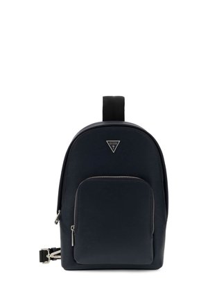 Sac à dos compact noir avec poche zippée à l’avant et logo Guess argenté en haut au centre, présenté sur fond blanc.