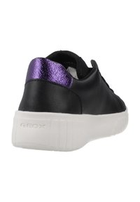 Zapatilla negra con un detalle brillante morado en el talón, suela blanca texturizada y parte superior de cuero liso. Nombre de la marca "GEOX" en el costado.