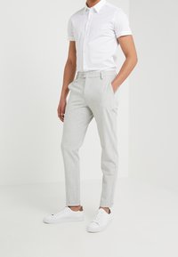 Lichtgrijze op maat gemaakte broeken van een gestructureerde stof, met zijzakken, een knoopsluiting en opgerolde mouwen, gecombineerd met een wit korte mouwen overhemd en witte sneakers.