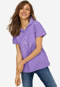Sudadera morada con capucha y mangas cortas, que presenta un diseño gráfico blanco en la parte delantera, combinada con unos jeans de mezclilla azules.