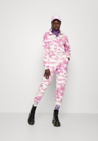 Mola de treino em tie-dye rosa e branco com uma parte superior de meia abertura, cós elástico e um gorro correspondente. Botas de combate pretas e acessórios em camadas.