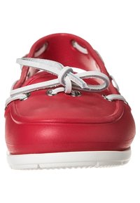Chaussure bateau en caoutchouc rouge avec lacets blancs, œillets en métal argenté, bout arrondi et détails découpés sur les côtés. Fini de surface texturé. Semelle blanche.