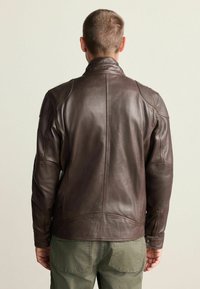 Braune Lederjacke mit hohem Kragen, strukturierten Schultern und Akzentnähten. Glatte Textur, taillierte Passform und leicht geschwungener Saum.