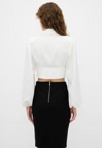 Blusa blanca recortada con mangas largas abullonadas, combinada con una falda lápiz negra con cierre de cremallera en la parte posterior. Tejido suave, diseño minimalista.