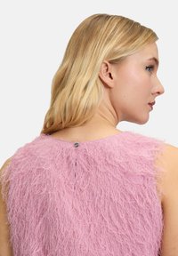 Haut sans manches rose en tissu texturé avec des franges. Doté d'une fermeture à bouton dans le dos et d'un col rond.