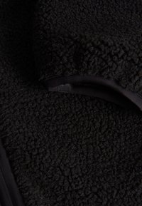 Zwarte fleece stof met een gestructureerd, pluizig oppervlak en gladde zwarte afwerking. Het patroon is zacht en uniform door het gehele materiaal.