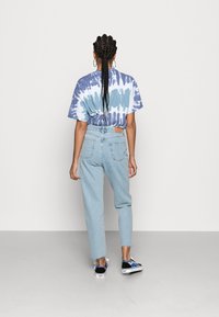 Camiseta tie-dye en azul y blanco, combinada con jeans de tiro alto en azul claro. Presenta un ajuste holgado y un parche de cuero con la marca en la parte trasera.