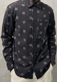 Zwarte blouse met subtiel crèmekleurig bloemmotief, gemaakt van zacht stof, met lange mouwen en een borstzak.