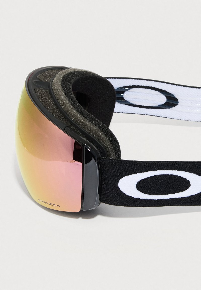 Lunettes de ski avec une lentille courbée teintée en ambre, monture noire et sangle réglable noire et blanche arborant un grand logo ovale.