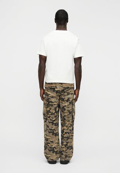 Λευκό κοντομάνικο t-shirt συνδυασμένο με φαρδιά cargo παντελόνια καμουφλάζ. Υφασμα με υφή, μεγάλες πλαϊνές τσέπες και χαλαρή σιλουέτα.