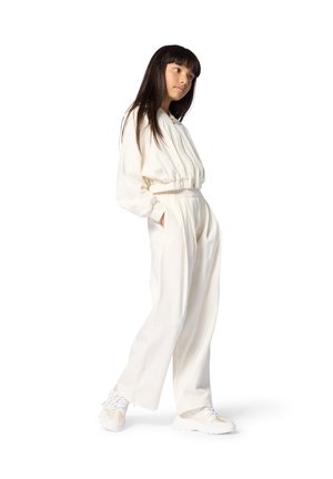 Witte jumpsuit met elastische tailleband en boorden, uitgevoerd met een rits en zijzakken; gecombineerd met lichtgekleurde, getextureerde sneakers.