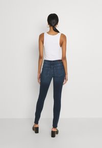 Höga mörkblå skinny jeans i denim, med två bakfickor och en slät yta. Kombineras med en vit ärmlös topp.