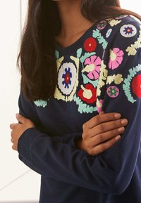 Felpa navy con ricami floreali colorati in rosa, rosso, verde e blu. Tessuto morbido con scollo rotondo e maniche lunghe.