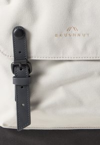 Doughnut bag in light gray canvas with black leather strap and hardware. Features subtle branding and precise stitching details.