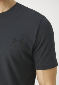 T-shirt in cotone nero con maniche corte, caratterizzato da un discreto logo Under Armour sul petto. Tessuto liscio e scollatura a girocollo standard.