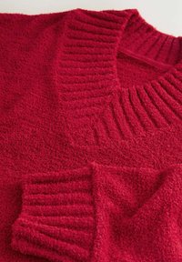 Czerwony sweter z teksturowanej wełny z prążkowanym kołnierzem i mankietami. Materiał wydaje się miękki i puszysty, z głębokim dekoltem w kształcie litery V.