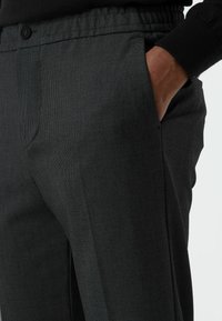 Zwarte slim-fit broek met een gestructureerde stof, elastische tailleband, zijzakken en een knoopdetail aan de taille.
