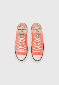 Orange canvas sneakers with white laces and rubber soles, featuring a black toe cap and branding on the tongue and outer side.