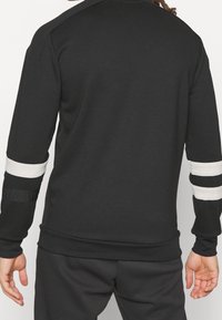 Felpa nera con strisce orizzontali bianche sulle maniche, design aderente, polsini e orlo a coste, realizzata in tessuto liscio.