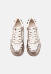 Pár bílo-bežových kožených tenisek s tkaničkami, perforovanou špičkou a hnědými gumovými podrážkami na bílém pozadí.