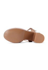 Sola in gomma color beige di una scarpa con superficie testurizzata e una lieve curva, caratterizzata da una fascia color pelle e una fibbia regolabile.