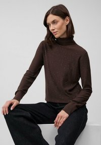 Pullover a collo alto marrone con una finitura texture, caratterizzato da sottili luccichii, abbinato a pantaloni neri larghi. Ambientato su uno sfondo neutro.