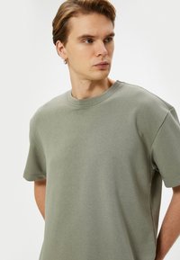 Camiseta de algodón verde claro con cuello redondo, mangas cortas y corte relajado. La tela tiene una textura suave con detalles de costura mínimos.