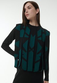 Schwarzer und türkisfarbener Pullover mit geometrischem Design, vertikalen Panels, langenÄrmeln und Rundhalsausschnitt. Sichtbare Details aus strukturiertem Stoff.
