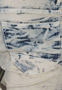 Denim tkanina s svijetlom podlogom i tamnoplave mrlje. Sadrži stražnji džep s vidljivim detaljem šivanja.