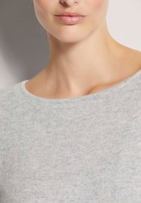 Hellgrauer Pullover mit weicher Textur, der einen weiten Ausschnitt und ein dezentes gesprenkeltes Muster aufweist. Eng geschnitten am Hals und Schlüsselbein.