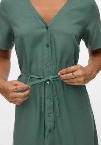 Abito verde a maniche corte con scollatura a V, chiusura con bottoni e cintura legata in vita. Tessuto morbido e vestibilità rilassata.